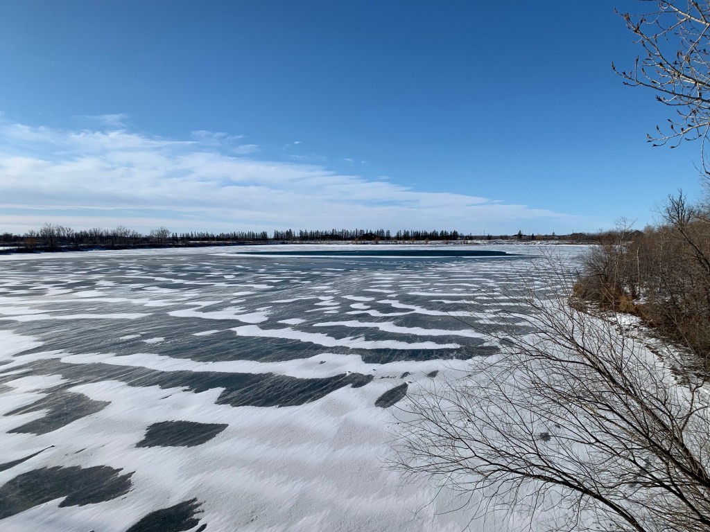 Picture of a lake with snow and ice on it. There are trees in the background.